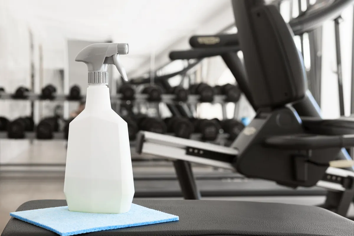 Sprühflasche und Tuch auf einer Trainingsbank im Fitnessstudio